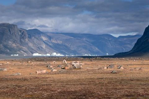 Icebergs in the distance float in the waters of remote arctic fjord in dramatic Stock Photos