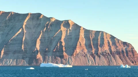 Icebergs float in calm water as the sun rises over the mountains in Greenland Vídeo Stock 331303995