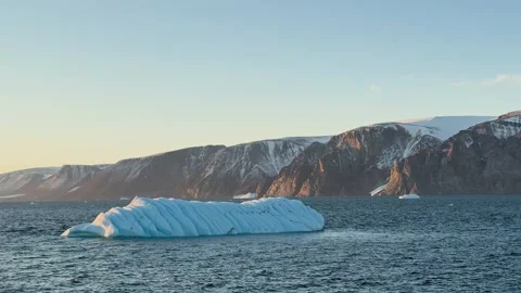 Icebergs float in calm water as the sun rises over the mountains in Greenland Vídeo Stock 331303996
