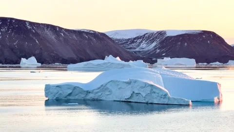 Icebergs float in calm water as the sun rises over the mountains in Greenland Vídeo Stock 331303999