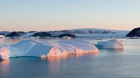 Icebergs float in calm water as the sun rises over the mountains in Greenland Vídeo Stock 331304003