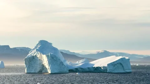 Icebergs float in calm water as the sun rises over the mountains in Greenland Vídeo Stock 331304004