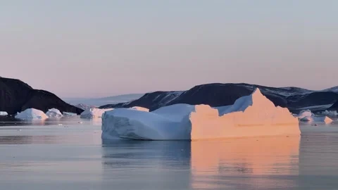 Icebergs float in calm water as the sun rises over the mountains in Greenland Vídeo Stock 331304006