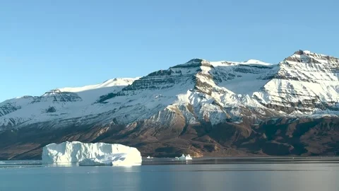 Icebergs float in calm waters of a glacier lagoon surrounded by mountains at sun 스톡 동영상 317930675