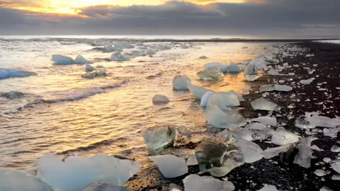 Icebergs shining on a black beach during golden hour. Sunrise on Diamond Beach Stock Footage 167333384