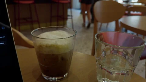 Iced coffee and empty water glass on cafe table with blurred interior seating in Stock Footage 345764293