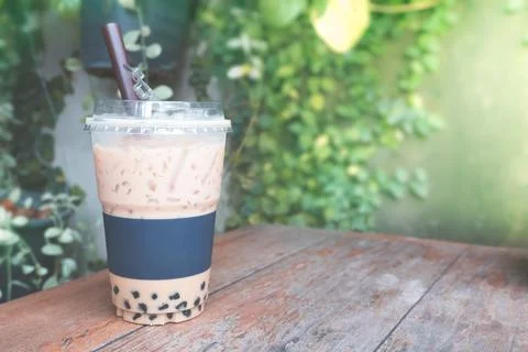 Iced coffee bubble with plastic takeaway glass on the wood table at the garde Stock Photos