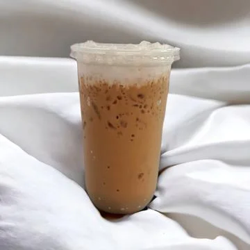 Iced coffee in a clear plastic cup topped with milk foam on top. There is a.. Stock Photos