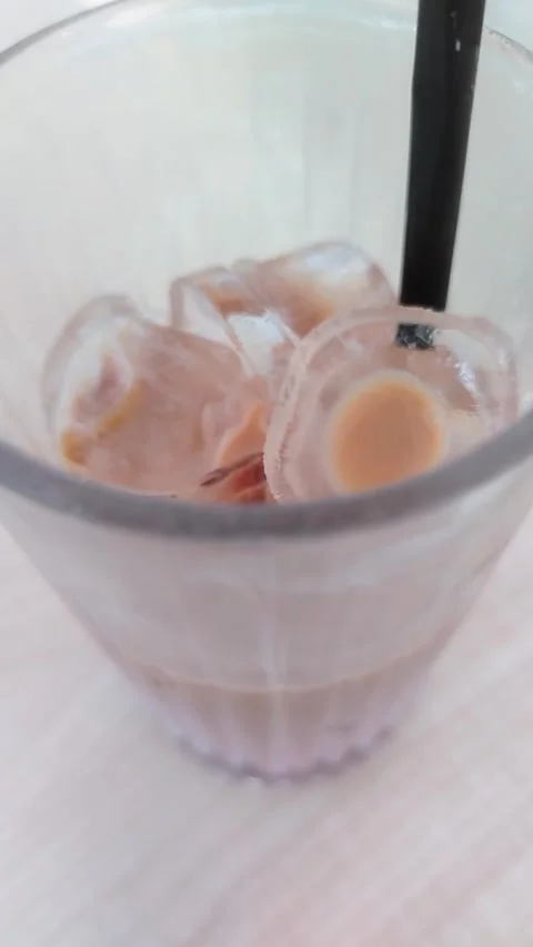 Iced coffee drink with ice cubes and black straw in clear glass on wooden table Video stock 340557473