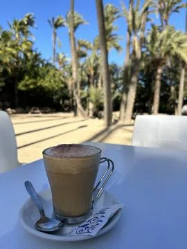 Iced coffee latte on a white table with tropical palm trees in the background Stock Photos