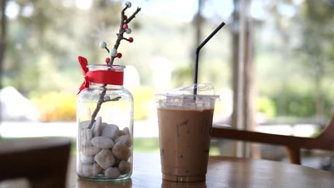Iced Coffee in Plastic Cup on Cafe Table with Natural Light and Cozy Background Stock Footage 325237395