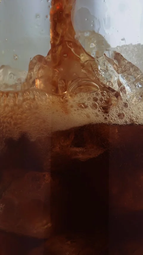 Iced coffee pouring over crystal ice cubes in tall glass, rich amber swirls, Stock Footage 314612567