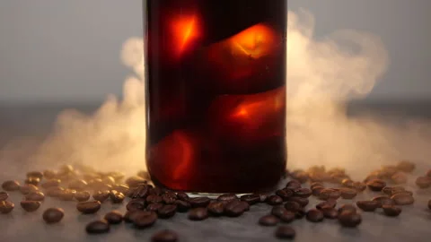 Iced coffee with steam in slow motion and coffee beans on table Stock Footage 134660437