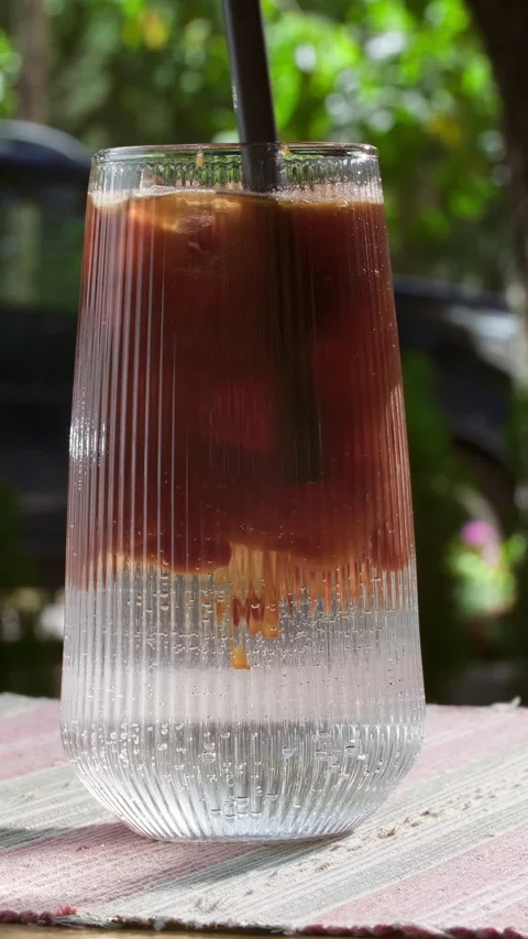 Iced coffee in summer on blurred greenery background. Stirring layered espresso Stock Footage 314457550