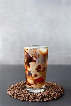 Iced coffee in a tall glass with cream and coffee beans around tumbler Stock Photos
