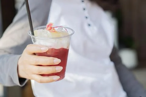 Iced fruit tea in the hands of a young woman while relaxing in a cafe with .. Stock Photos