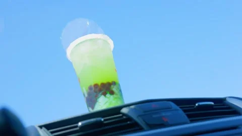 Iced green bubble tea cup on car dashboard against blue sky Stock Footage 338028635