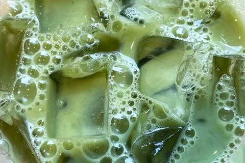 Iced matcha latte close up, texture of refreshing tea with transparent ice cubes Stock Photos