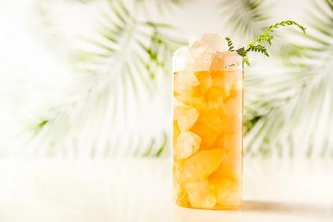 Iced tea with crashed ice in a transparent tall glass on tropical background Stock Photos