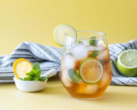 Iced tea with ice, lemon, lime and mint in a glass on a yellow background Stock Photos