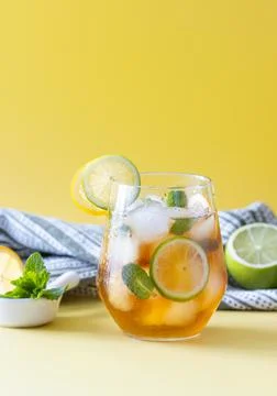 Iced tea with ice, lemon, lime and mint in a glass on a yellow background Stock Photos