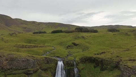 Iceland Aerial Drone Slow Pullback and tilt down from green hills to waterfall Stock Footage 318045410