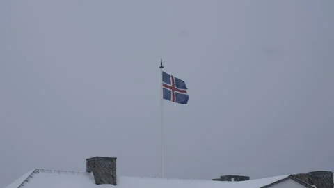 Icelandic flag waving in the wind over a snowy rooftop during a blizzard. Stock Footage 329925234