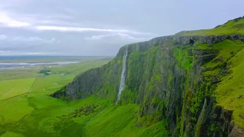 Icelandic waterfall cascades down massive green cliff side under overcast sky Stock Footage 343696184