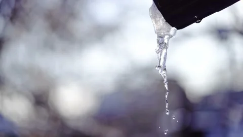 Icicle melts on warm day, stream of water runs over it and drops fall Stockbeeldmateriaal 223369031