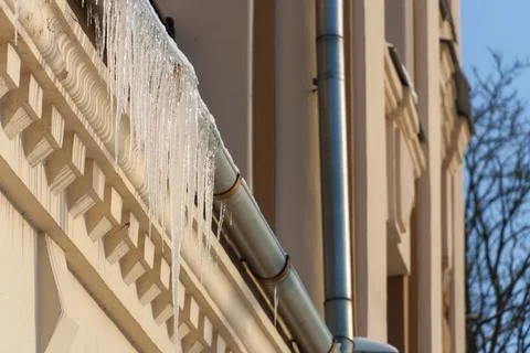 Icicles are hanging on the ventilation pipe. Shiny metal pipes on the facade  Stock Photos