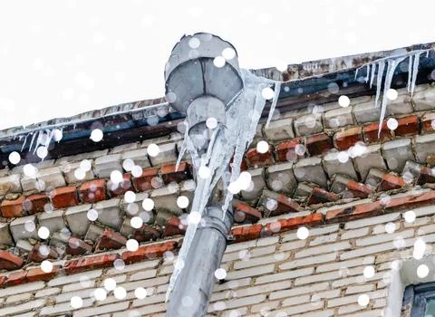 Icicles dangle from a metal gutter as soft snowflakes fall, creating a serene Stock Photos