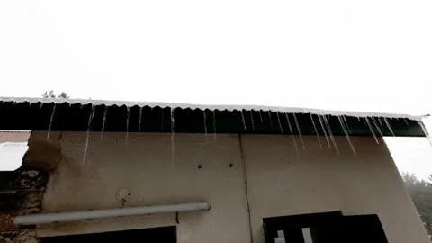 Icicles form on a rooftop in a snowy landscape during wintertime Stock Footage 301602587