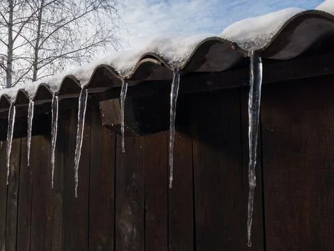 Icicles hang from the eaves during the winter day, plank buildings Stock-Fotos