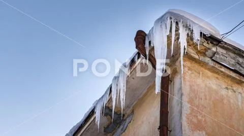 Icicles hang from roof of building. Danger for passers, threat of death and Stock Photos
