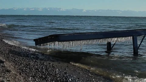 Icicles hanging over the water. Waves on lake Baikal, Siberia, wooden pier. Stock Footage 86434172
