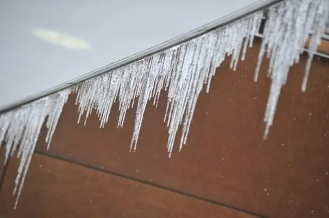 Icicles hanging from rain gutter Stock Photos