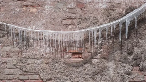 Icicles hanging from a wire in front of an old brick wall background Stock Footage 346239373