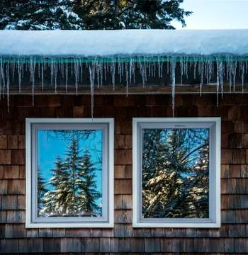 Icicles on house with trees reflections in windows Stock Photos