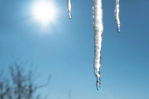Icicles melt and drip in the spring against the blue sky with the sun and sun Stock Photos