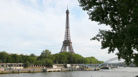 The iconic Eiffel Tower soaring high above the Seine River, framed by lush green Stock Footage 336363059