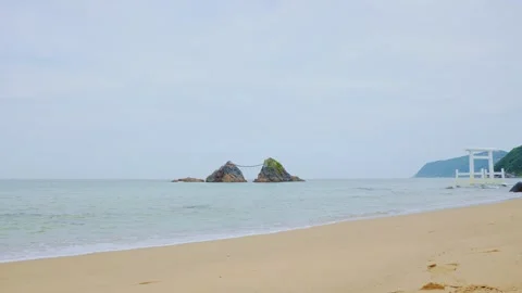 Iconic white Torii gate and Meoto Iwa rocks on empty beach in Japan Stock Footage 338194019