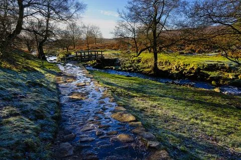 Icy cobbled path leads down to a wooden bridge across Burbage Brook. Foto stock