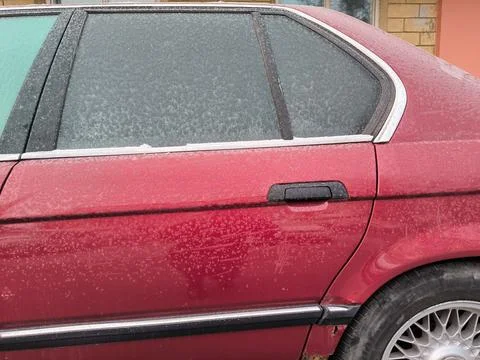 Icy layer on the back door window of a red car. Stock Photos