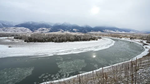 Icy River flowing around bend below mountains Stock Footage 327689703