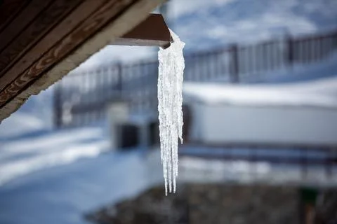 An icy stalactite hangs from a gutter. Ice water comes out of a gutter Stock Photos