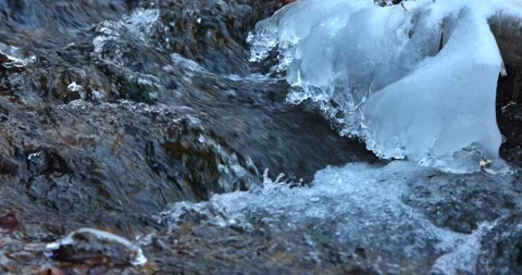 Icy stream captured in winter; water flows rapidly around frozen formations. The Stock Footage 324866089