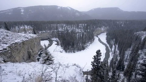 Icy winter river winds through canyon valley in snowstorm Stock Footage 85503897