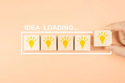 Idea loading concept. Hand putting wooden cube block shape with lightbulb. Co Stock Photos