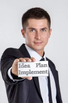 Idea - Plan - Implement - Young businessman holding a white card with text Foto stock