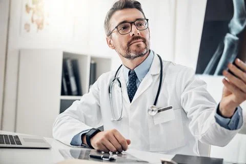 Identifying the root of the problem. a focused doctor looking at an x-ray while Stock Photos